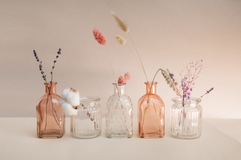 Five decorative glass bottles with dried flowers in a minimalist indoor setting.